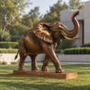 Realistic bronze elephant sculpture with raised trunk displayed on a manicured garden lawn beside trimmed hedges and pale stone architecture