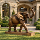 Realistic bronze elephant statue with raised trunk displayed on a manicured lawn in front of a luxury stone estate entrance