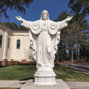 White marble Sacred Heart of Jesus statue with outstretched arms and flowing robes outside a church.