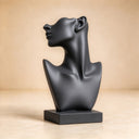 Depicted against a neutral studio backdrop, this matte black abstract bust highlights sleek geometric contours and a serene upward gaze for hotel art collections.