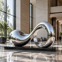 Abstract stainless steel wave sculpture SS-029 displayed on a black stone plinth in a modern luxury hotel lobby with natural daylight