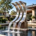 Stainless steel fountain sculpture SS-031 with three curved metal blades cascading water into a reflecting pool in a modern luxury hotel garden