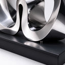 Close view of the interlocking lower curves and black base of an abstract stainless steel loop sculpture.