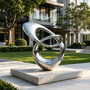 Contemporary stainless steel loop sculpture installed in a luxury landscape with modern architecture and outdoor artistic design