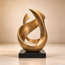 Rising from a dark base, two gold-finished bronze ribbons reveal broad curved surfaces, slender edges and tapered tips in a studio setting.