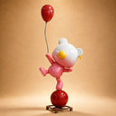 The fiberglass bear sculpture pairs rounded white ears and a pink body with yellow facial details, a red balloon and a spherical base in a studio view.