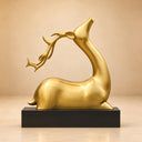Studio shot of a gold reclining gazelle sculpture with long curved horns on a black base against a light background, showcasing its metallic finish and elegant posture for art decor product display and reference.

