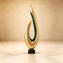 Studio shot of a modern abstract gold teardrop sculpture with a green inlay accent and a black base against a beige background, highlighting its polished metallic finish for art decor product display and reference.