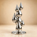 Studio shot of a polished stainless steel stacked teardrop sculpture on a circular base against a beige background, highlighting its reflective metallic surface and modern abstract design for art decor product display.