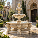 A three-tier beige stone fountain featuring a baroque-sculpted basin, designed as a classic water feature for a chapel courtyard.