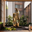 A large vertical abstract bronze sculpture featuring paired rising forms and circular openings, placed among plants and gravel in a modern courtyard. Model BB-033.