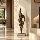 Vertical abstract bronze sculpture displayed in a modern hallway with sunlight casting soft shadows on the walls, suitable for luxury entryway and interior art decoration.