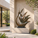 Resting on a dark rectangular base, the bronze bird sculpture opens into tapered, fan-like feathers within a landscaped villa courtyard.