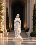 Praying Virgin Mary statue carved from white marble and centered before a limestone chapel entrance.